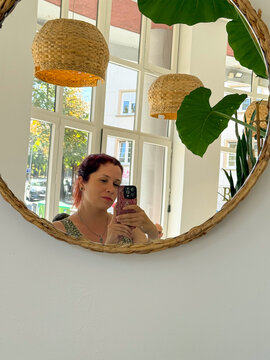 Woman taking mirror selfie in bright cafe interior. Natural light, reflection, and candid everyday lifestyle moment.
