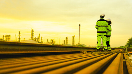Witness the immense scale of petrochemical giants. Two engineers observe the sprawling industrial complex at sunset, a symbol of powerful, vast operations and global energy.