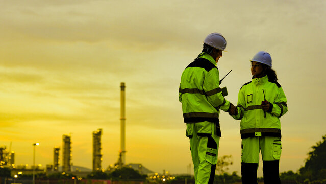 Energy professionals plan for the future at a refinery. The diverse team uses technology to monitor sustainable operations during a beautiful golden sunset.