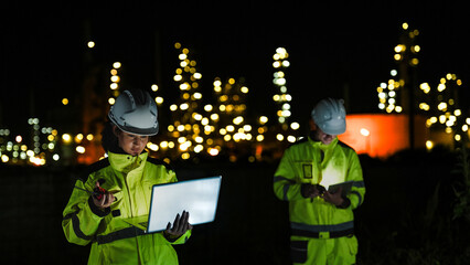 Petrochemical engineers in PPE conduct a night inspection at a refinery. They use a laptop and...