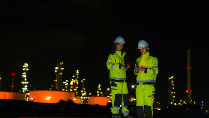 Energy professionals ensure 24 7 operations at a refinery. The team uses digital technology on a laptop to monitor sustainable production at night.