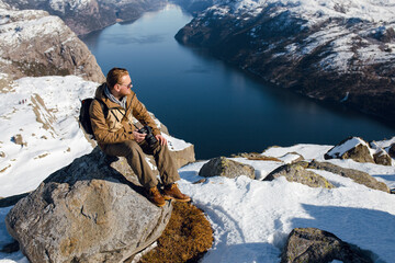 Man with Camera on Snowy Cliff Overlooking Fjord