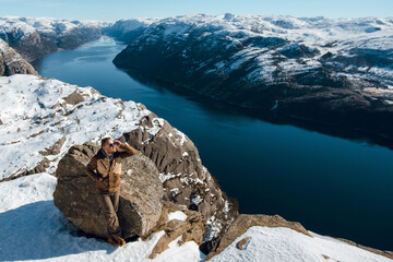 Man Enjoying Scenic View from Snowy Cliff Overlooking Fjord