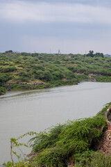 scenic view of calm river flowing through green hills under cloudy sky