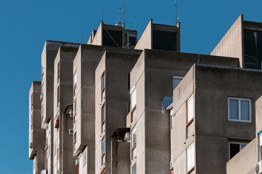 High-rise brutalist concrete apartment building in Belgrade with staggered balconies against a deep blue sky.