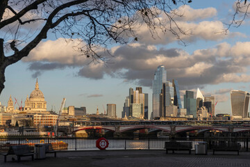 London, UK Panoramic view of the london skyline from the river thames, contrasting the dome of St. Paul's cathedral with the modern skyscrapers of the city, framed by a bare tree branch.