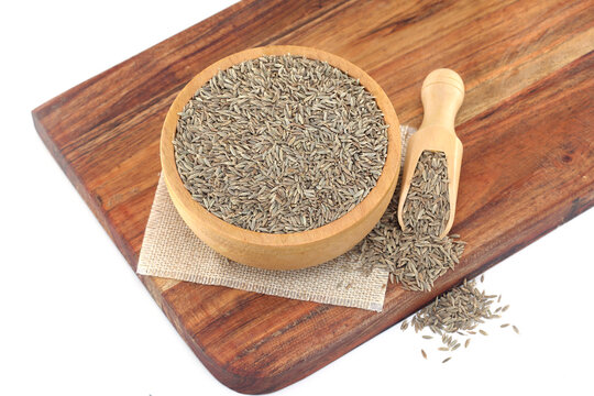 Fresh cumin seeds spilled out of wooden bowl and scoop on white background