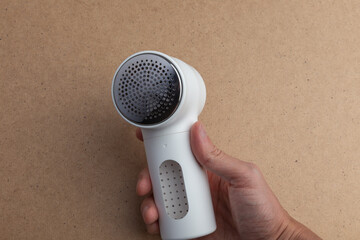 A compact white handheld lint remover is gripped by a person&rsquo;s hand