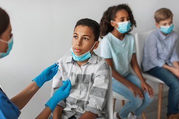 In a clinic, an African American boy sits calmly while a medical worker conducts a Covid-19 antigen...