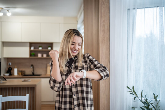 Happy woman checking smartwatch at home seeing success