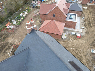 Low level drone inspection view of a new tiled roof and solar panel attached to a near completed family home on a British housing estate. A conservatory and glass lantern can be seen on the next house