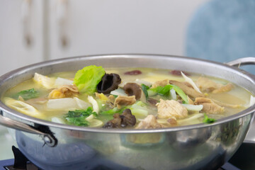 Chicken and vegetable soup with mushrooms and leafy greens simmering in stainless steel pot, warm homemade comfort food in kitchen
