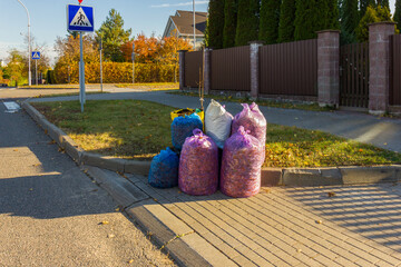 Colorful purple and blue trash bags neatly stacked along the sidewalk near the Pedestrian Crossing sign.
