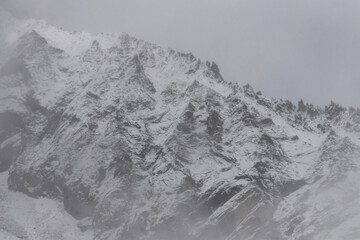 Snow covered rocky mountain ridge in misty winter landscape with dramatic texture and cold atmosphere