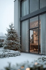 A modern glass-front home with tall windows is decorated with warm Christmas lights and snowy trees, while snow falls softly on the surrounding white garden