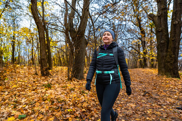 Mature woman hiking on path in forest on autumn day. Front view	