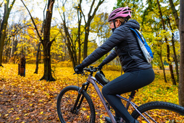 Beautiful middle-aged woman riding bicycle on path in forest in autumn. Side view