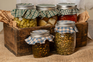 Food harvested and preserved by canning in glass jars. Potatoes, tomatoes, beans, salsa, and pumpkin seeds. Homemade gifts, self-sufficiency, National canned food month concept