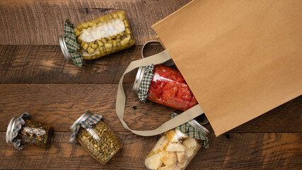 Food items preserved in glass jars spilling out of a brown, reusable shopping bag.