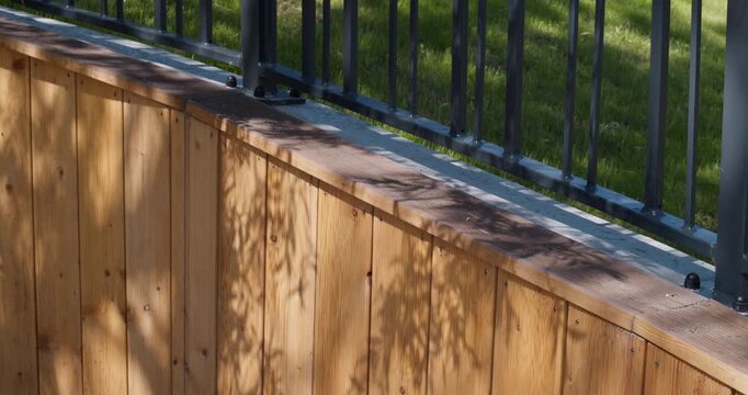 Close-up of a modern fence featuring vertical wood cladding and metal railing under sunlight. Contemporary small architecture and outdoor design concept.