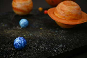 Handcrafted models of planets representing the solar system on a dark, textured background