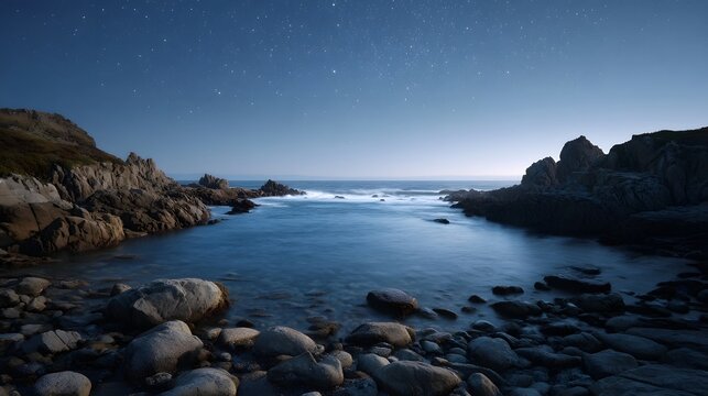 A serene rocky coastline under a clear starlit night sky with gentle ocean waves