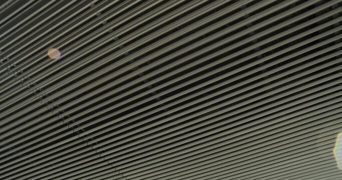 Minimalist exterior ceiling of an office building made with aluminum slats, contemporary architectural design highlighted by sunlight lens flare.