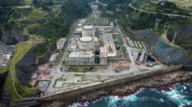 Aerial drone view of the abandoned Lemoiz nuclear power plant ruins on the Basque Country coast, Spain. The unfinished industrial complex with twin reactor domes sits between cliffs and the sea