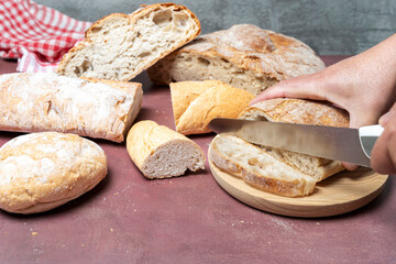 Hand holding a knife cutting a loaf of sourdough bread on a wooden board