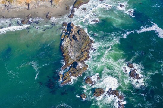 Aerial view of a rocky outcrop in turquoise ocean waves