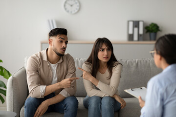Couple sits on a couch in a counselor's office, visibly upset. They are blaming each other for...