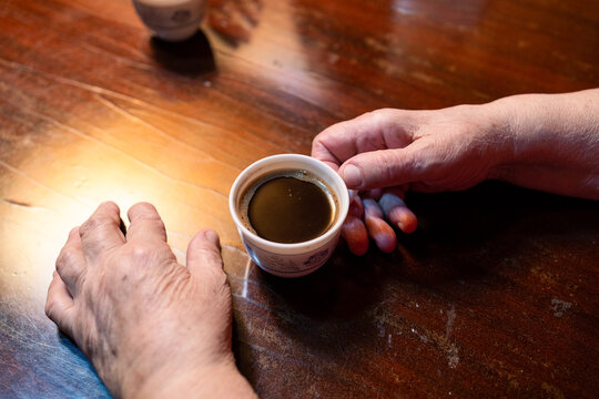 Elderly hands holding coffee cup on wooden table