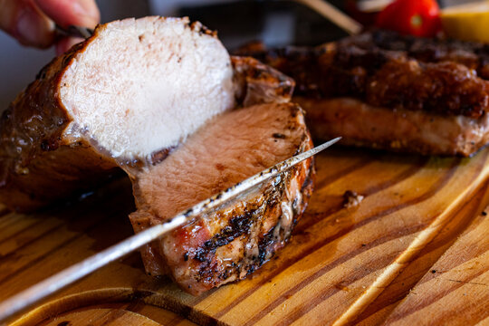 Hand cutting thick slices of grilled beef picanha off the bone on a wooden cutting board, - Powered by Adobe