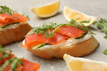 Tasty bruschettas with salmon, cream cheese, cucumber, arugula and lemon on grey table, closeup