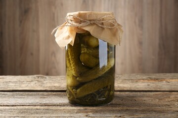 Pickled cucumbers in jar on wooden table