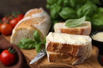 Slices of baguette with butter, basil, tomatoes and knife on wooden table, closeup
