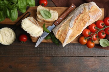 Slices of baguette with butter, basil, tomatoes and knife on wooden table, flat lay. Space for text