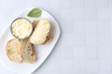Slices of baguette with butter and basil on white tiled table, top view. Space for text