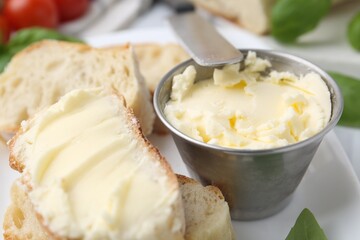 Slices of baguette with butter, basil and knife on white table, closeup