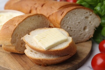 Cut baguette with butter, basil and tomatoes on white table, closeup