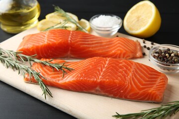 Pieces of salmon fillet, spices and lemon on black wooden table, closeup