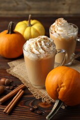 Tasty pumpkin latte with whipped cream in glass cups and ingredients on wooden table, closeup