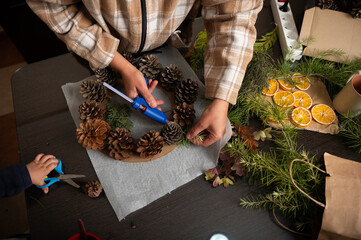 Family Crafting Christmas Wreath With Pinecones, Citrus And Greenery At Home