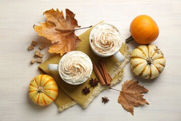 Tasty pumpkin latte with whipped cream, spices, leaves and fresh vegetables on white wooden table, flat lay