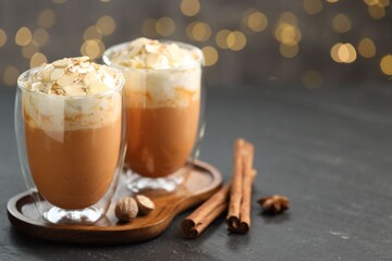 Tasty pumpkin latte with whipped cream and spices on black table against blurred lights, closeup. Space for text