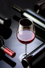 Glass and bottles of red wine on a black reflective background.