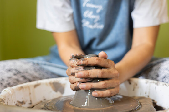 Close up of female hands shaping clay on pottery wheel in selective focus. Artistic handmade ceramic, learning pottery craft, creative process, traditional artisan skill, hobby and craftsmanship.