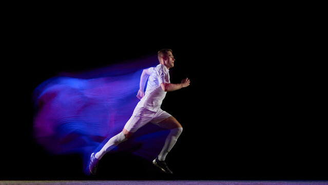 Soccer runner sprinting with purple blue trail effect on black background. Concept of physical energy, endurance, and motion technology for sportswear and performance brands.
