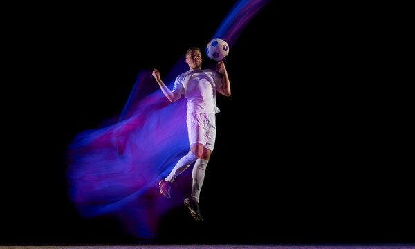 Football player jumping for header with glowing blue motion trail. Concept of sports action, human motion study, and creative visuals for fitness branding and event promotion.