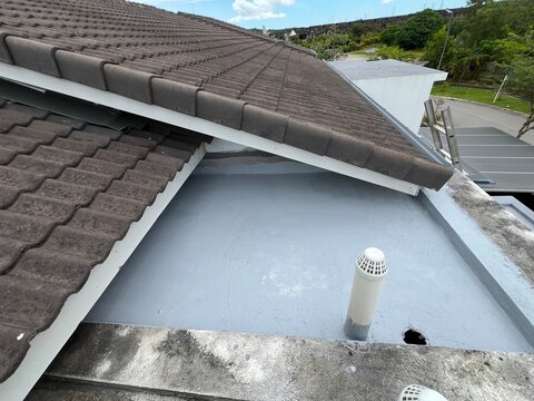 Waterproofed flat roof beside tile roof with vent pipe